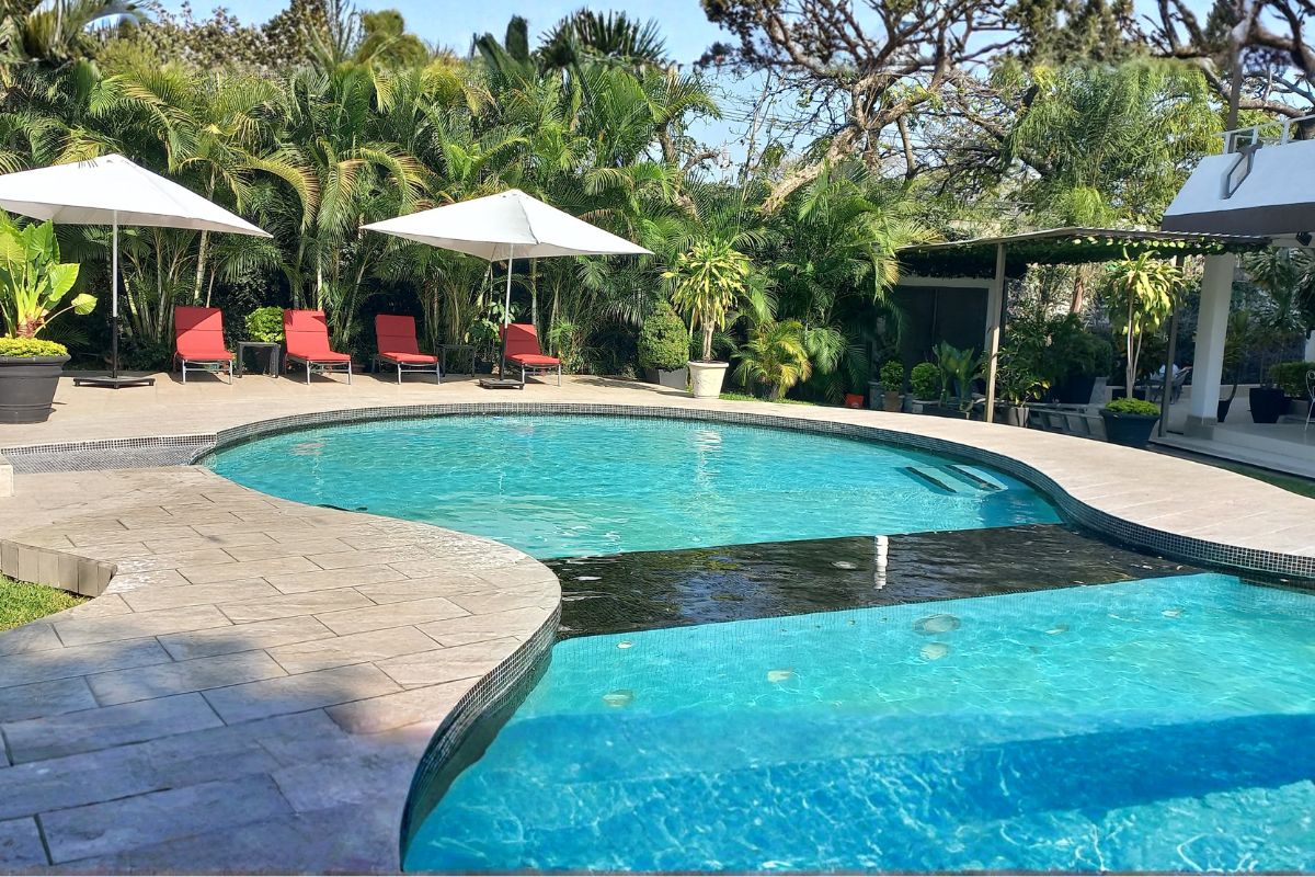 Alberca exterior en Allegra Suites con camastros rojos, sombrillas blancas y vegetación tropical.