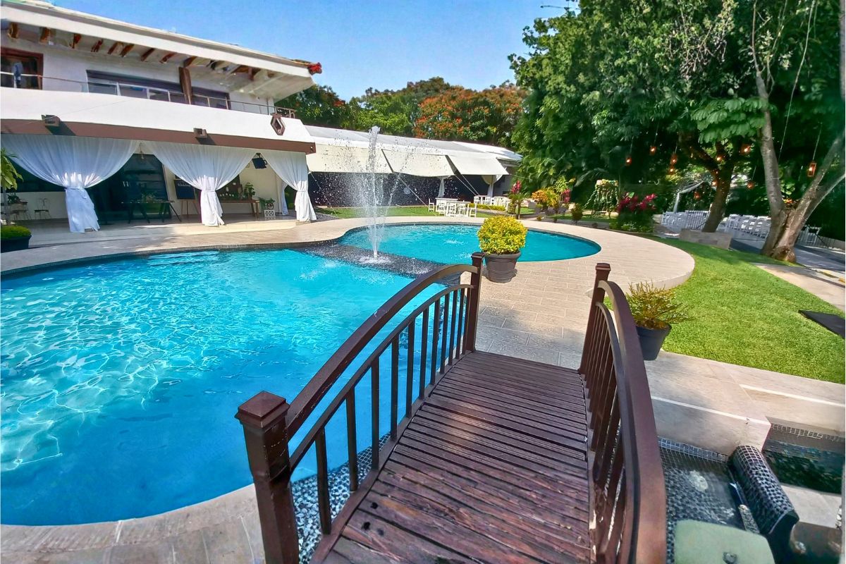 Alberca exterior en Allegra Suites con fuente central, puente de madera y carpa para eventos.