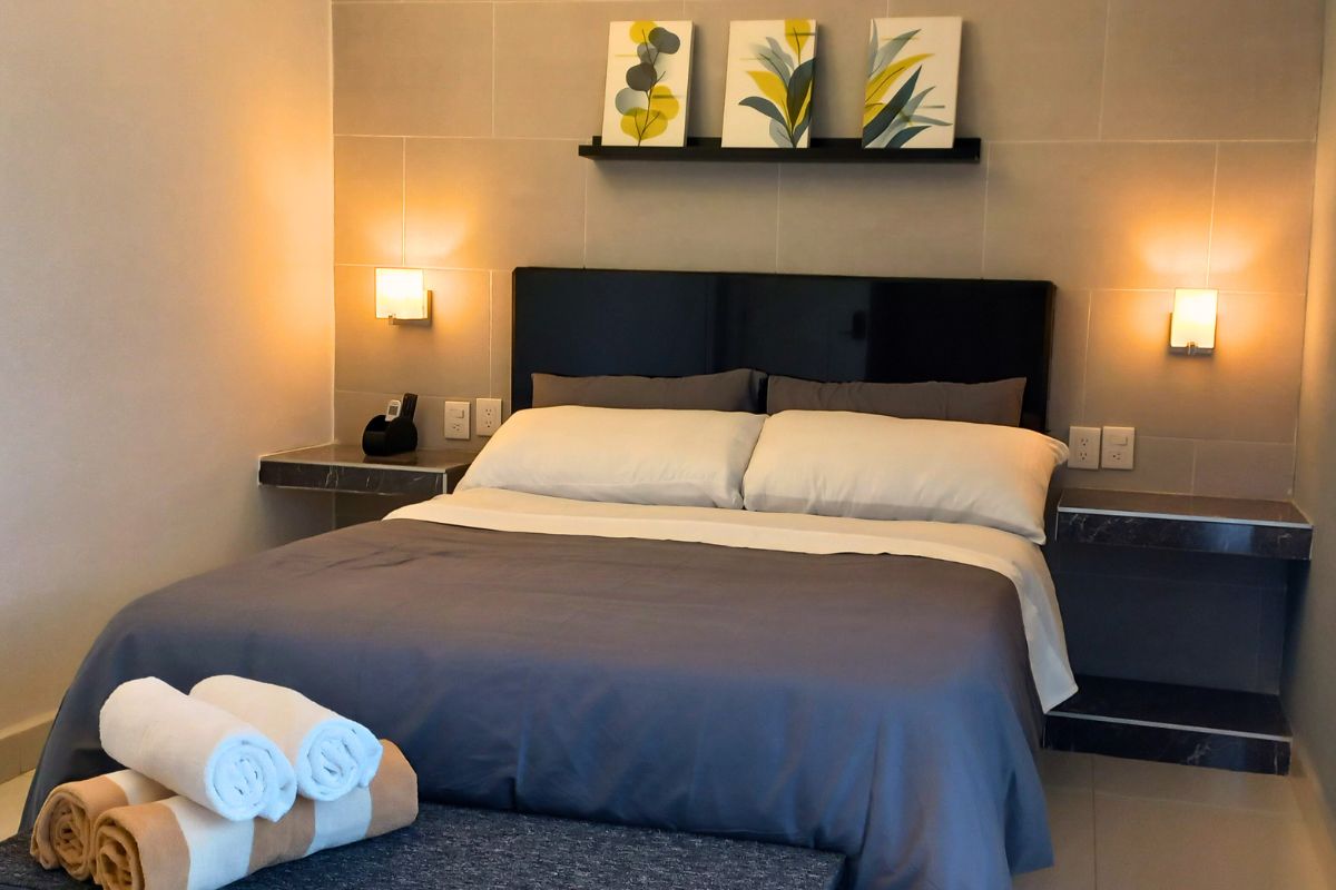 Recámara moderna en Allegra Suites con cama queen, decoración botánica y luz cálida.
