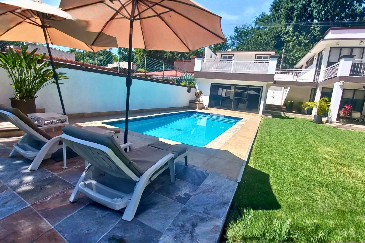 Área exterior en Eucalipto 26 con alberca, camastros, sombrillas y jardín privado.