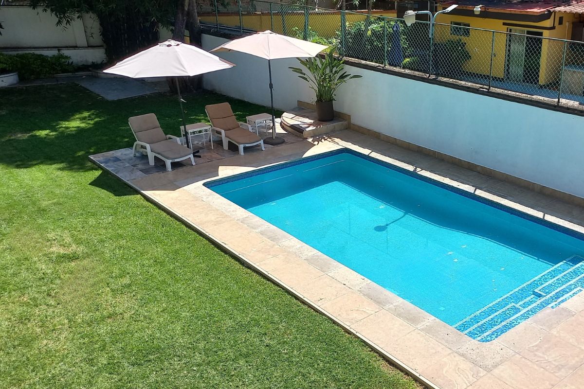 Área exterior en Eucalipto 26 con alberca, mesita bajo sombrilla y vegetación tropical.