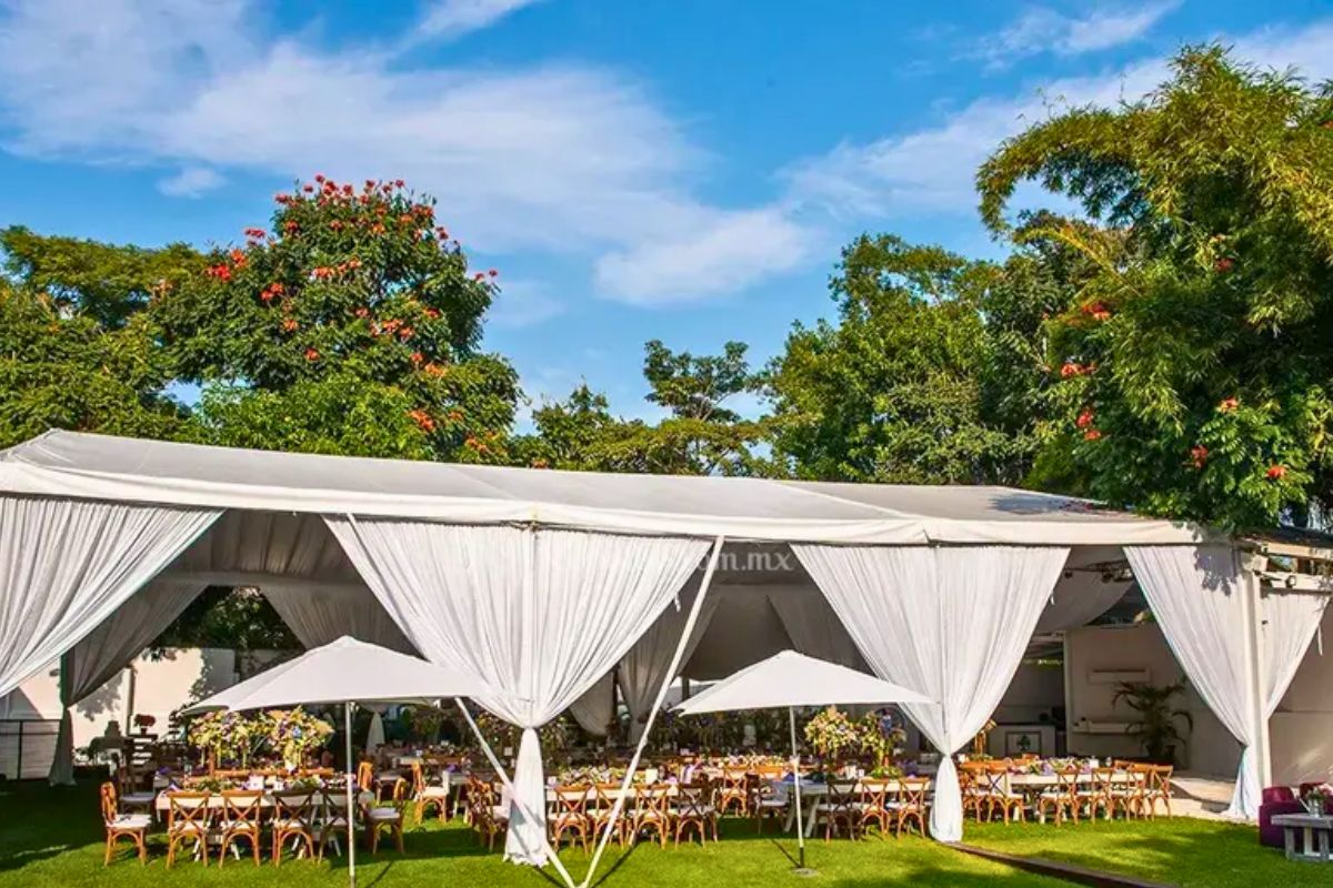 Jardín Allegra con carpa blanca, mesas de madera, sombrillas y entorno arbolado.