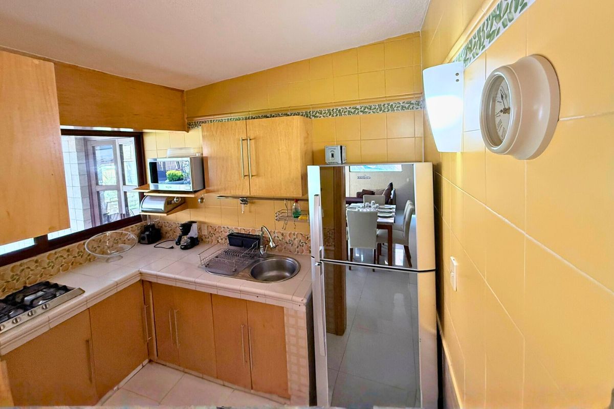Cocina en Las Fuentes 34-A con alacenas de madera, estufa, refrigerador y barra decorativa.