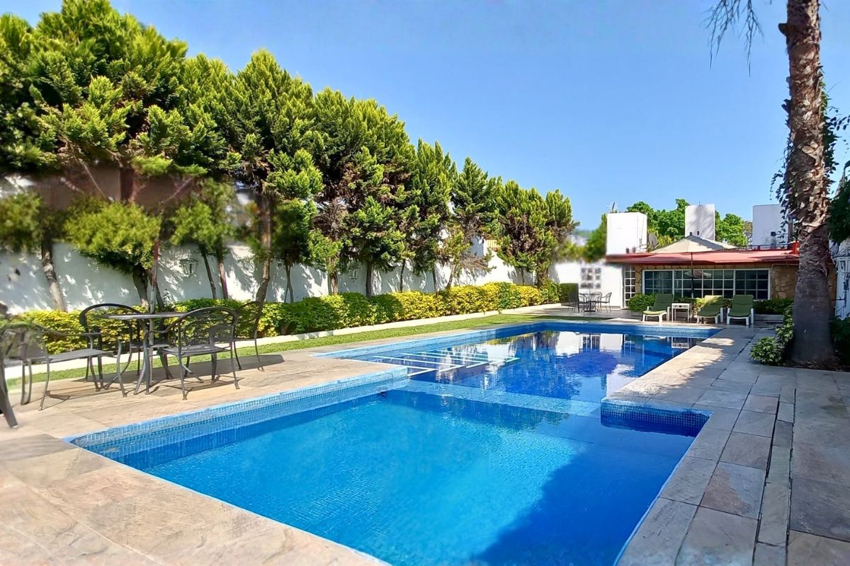 Área exterior en Pedregal 20 con alberca, camastros, sombrilla y terraza techada entre vegetación.