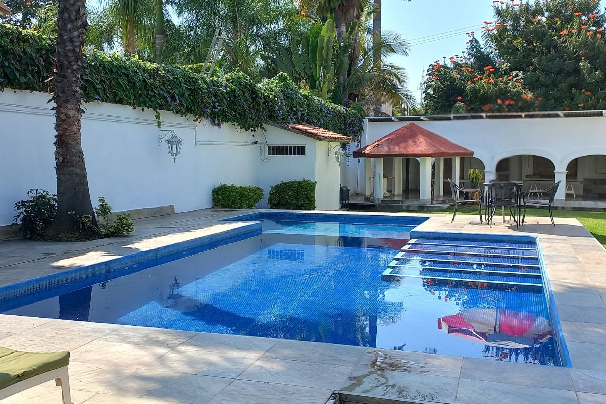 Área exterior en Pedregal 20 con alberca moderna, terraza techada y vegetación tropical.