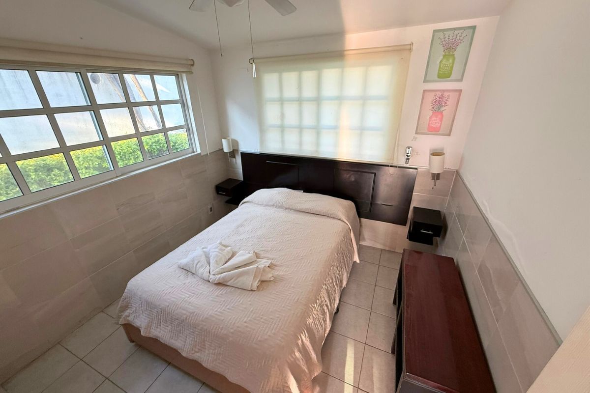 Segunda recámara con cama matrimonial en Pedregal 20 con cabecera de madera, decoración floral y luz natural.