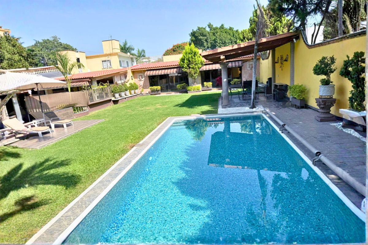 Jardín en Villa Las Fuentes con alberca, terraza techada y camastros bajo sombrillas.