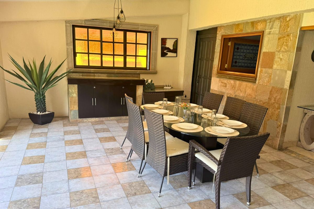 Comedor en Villa Las Fuentes con mesa ovalada de cristal, sillas de mimbre y decoración cálida.