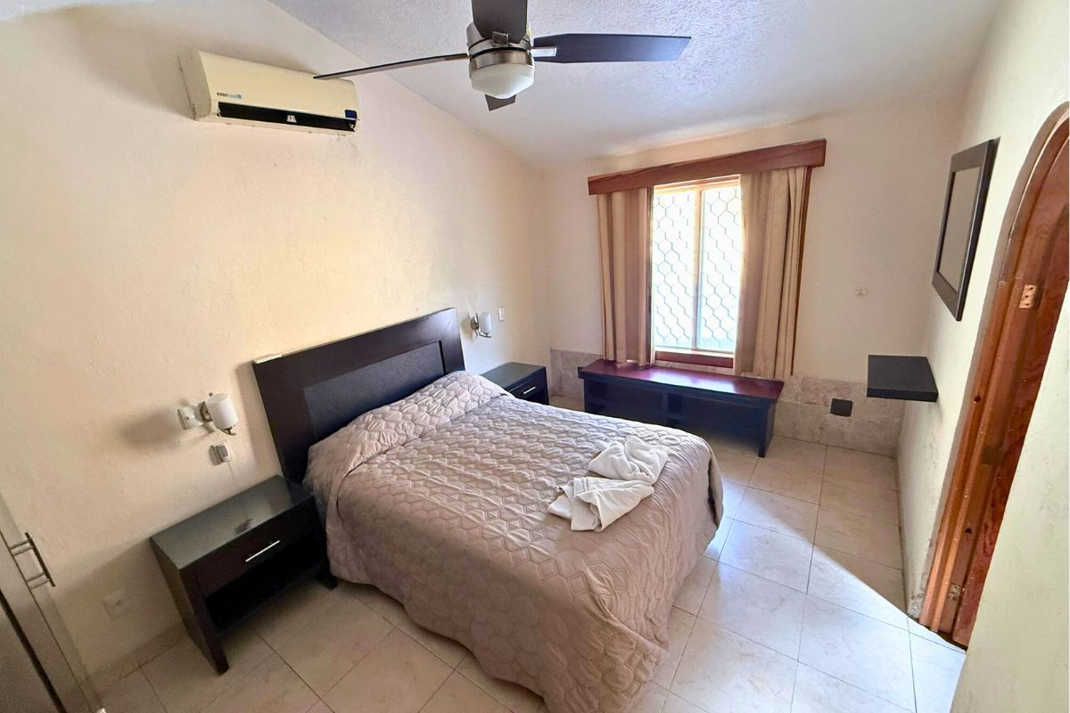 Recámara en Villa Las Fuentes con cama matrimonial, ventilador, aire acondicionado y espejo decorativo.