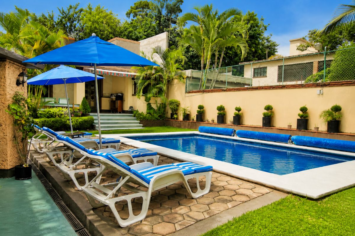 Camastros y sombrillas azules junto a la alberca de Villas Eucalipto rodeada de palmeras, Allegra Homes en Cuernavaca, Morelos