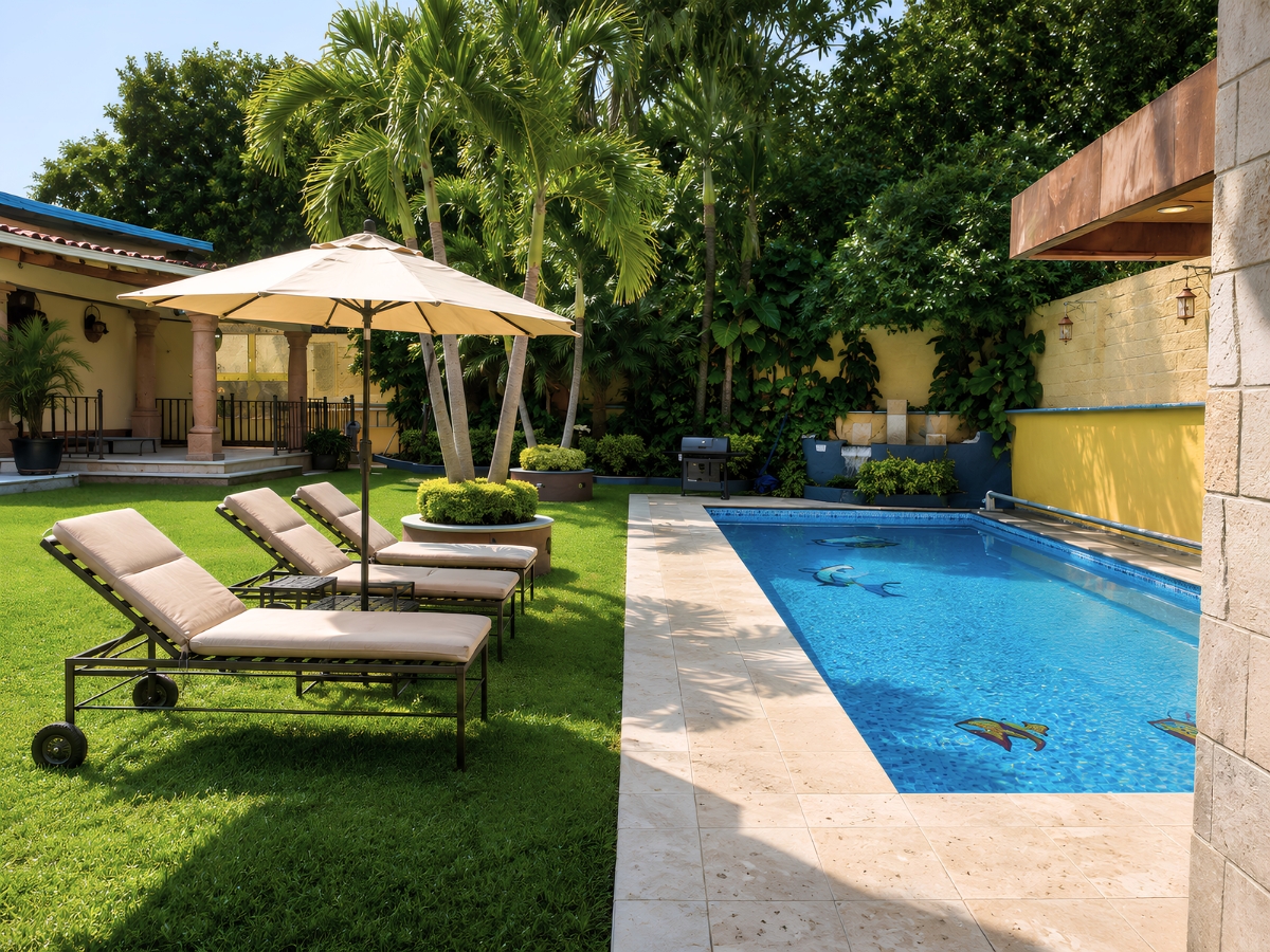 Jardín tropical con palmeras, camastros y alberca junto a muro amarillo, casa Las Fuentes 34-A en Cuernavaca