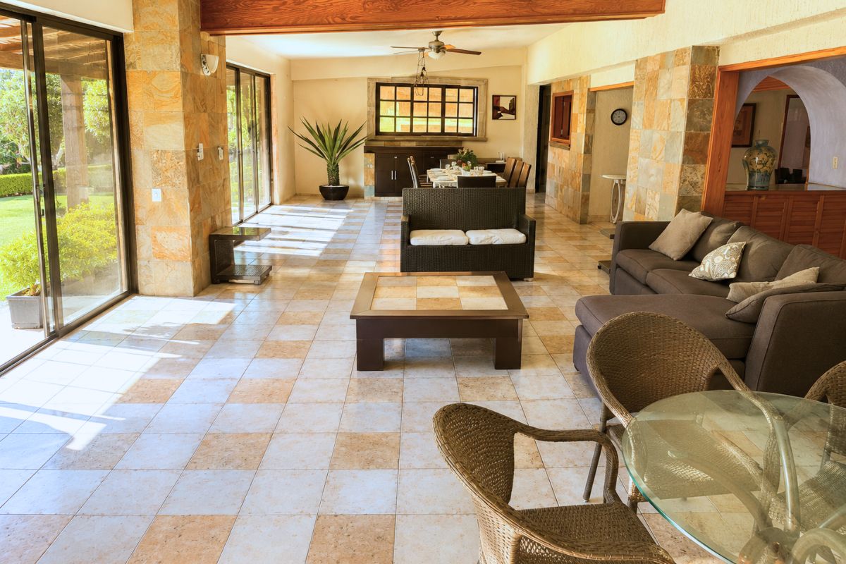 Sala amplia con ventanales al jardín y muebles de ratán en Villa Las Fuentes, Cuernavaca